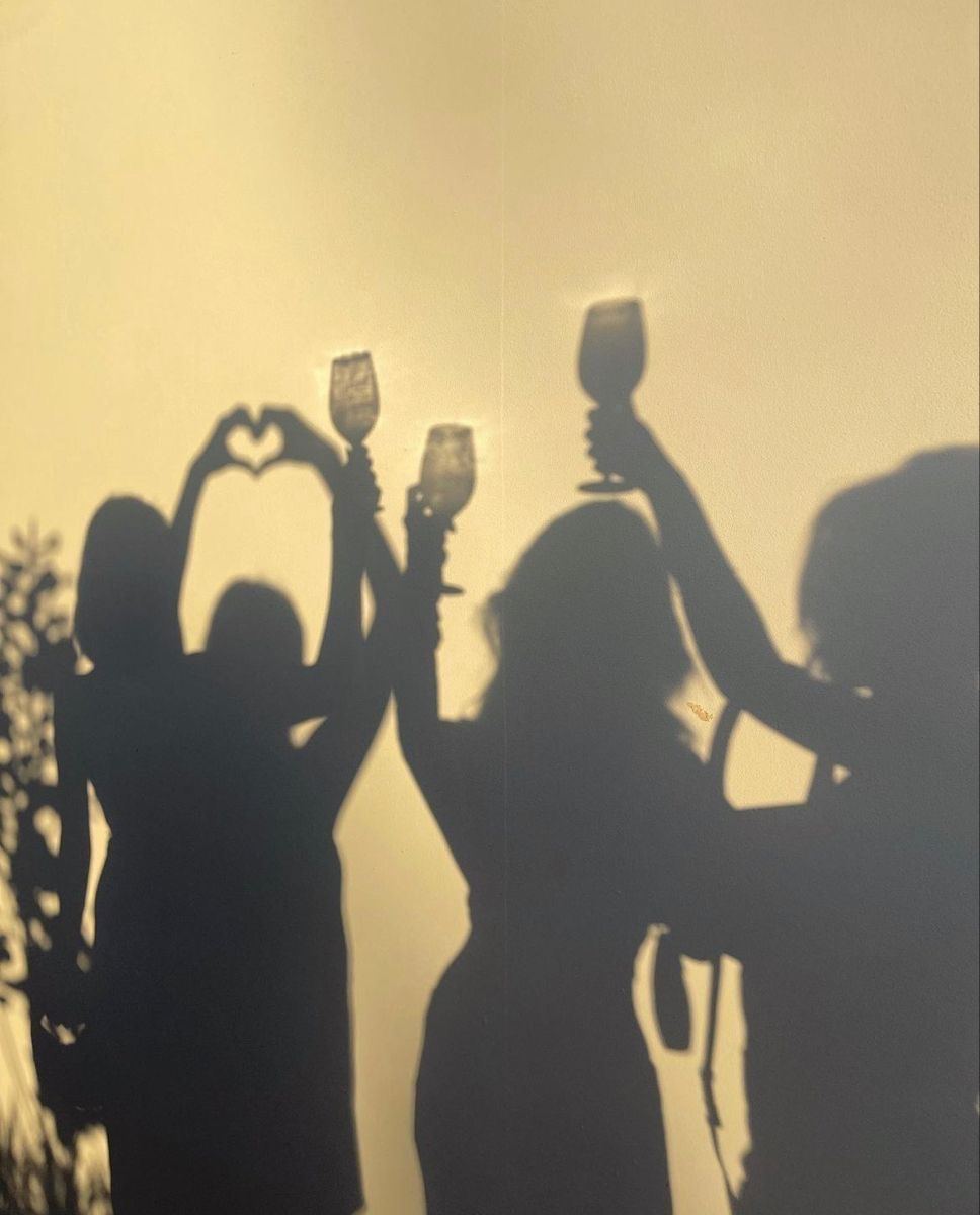 Les ombres de quatre amies qui lèvent leur verre sur un mur ensoleillé
