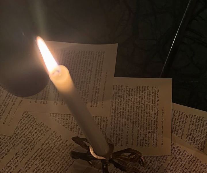 Une bougie allumée sur des pages de livre éparpillées